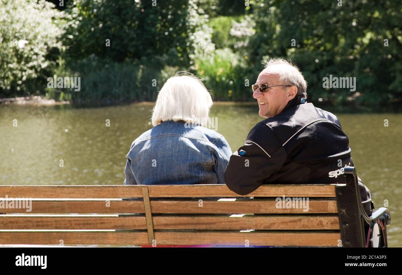 Vecchia coppia seduta su una panchina che si affaccia su un fiume Foto Stock
