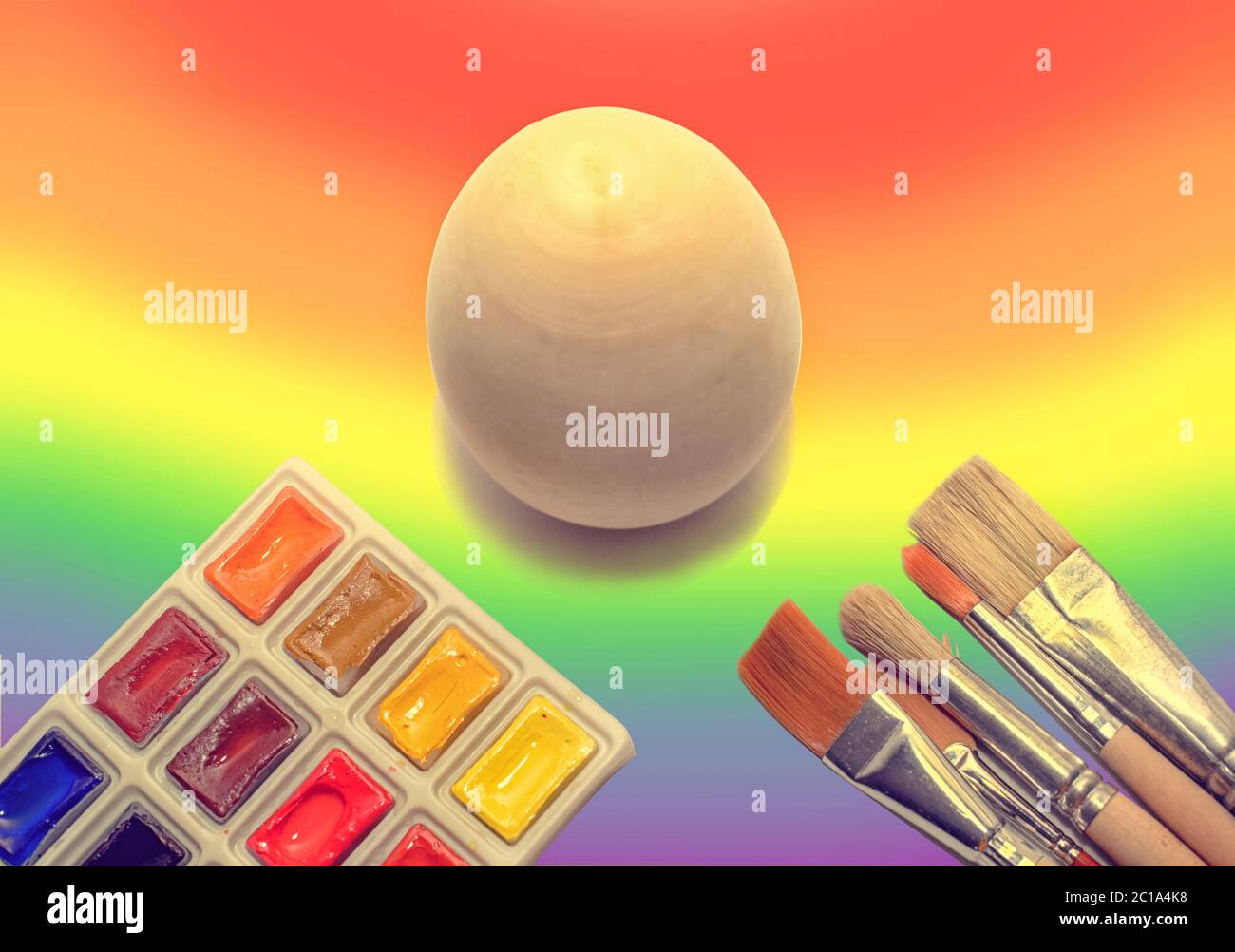 Non in legno dipinto di uovo sullo sfondo di un arcobaleno e un pennello con vernici, il concetto di colorare il mondo con vernici Foto Stock