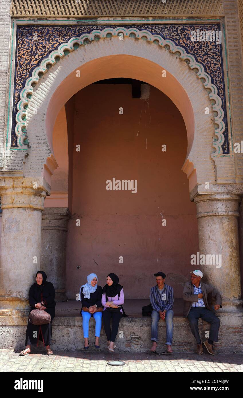 Meknes Marocco. La gente del posto siede sotto la porta medievale di Bab Mansour nel centro storico della città imperiale, uno dei suoi monumenti più importanti. Foto Stock