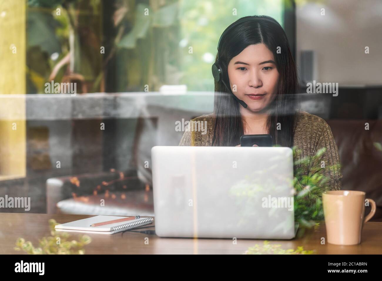 Donna aziendale asiatica che utilizza notebook e cuffie tecnologici per lavorare da casa in una casa al coperto tramite videochiamata, startup e business owner Foto Stock Donna aziendale asiatica che utilizza notebook e cuffie tecnologici per lavorare da casa in una casa al coperto tramite videochiamata, startup e business owner Foto Stock