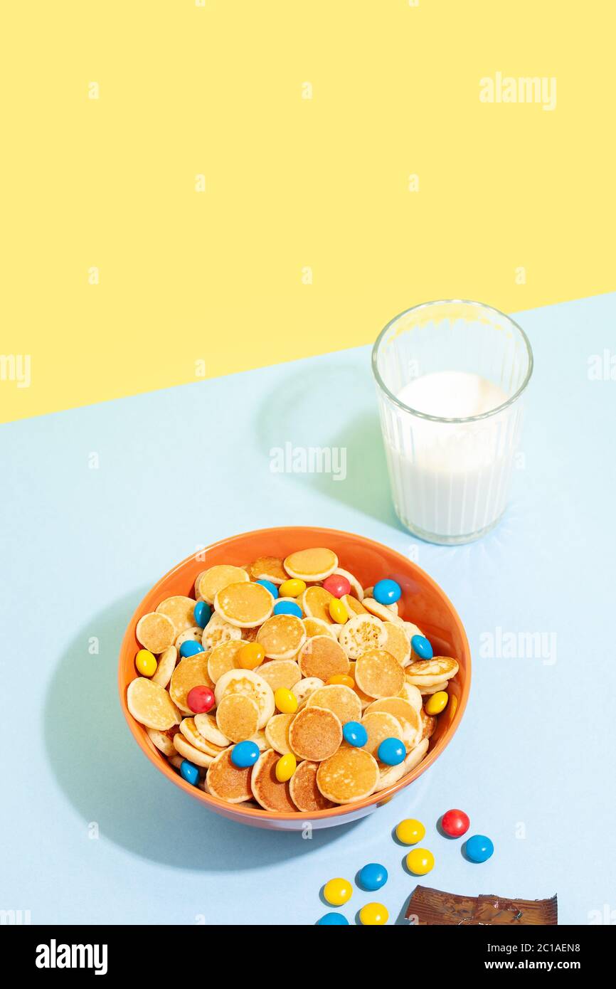 Terrina Orane con minuscoli porridge di cereali con pancake e latte su sfondo blu giallo. Gustosi piatti per la colazione alla moda Foto Stock
