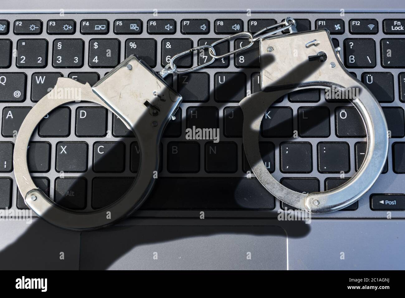 Manette giacciono sulla tastiera del computer e ombra scura di una mano che simboleggia il crimine informatico Foto Stock