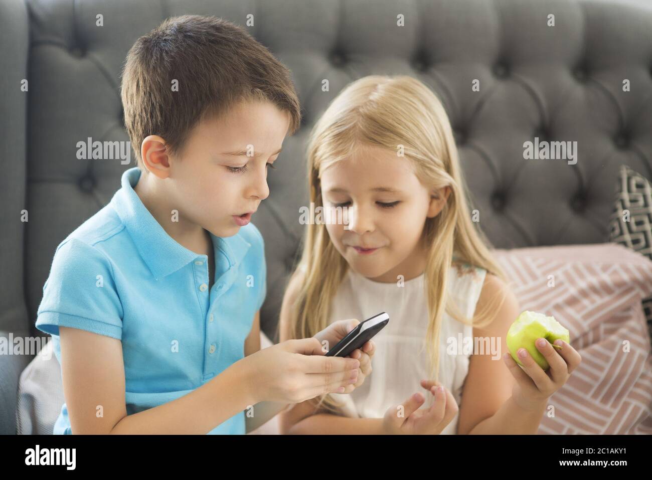 Fratello piccolo e sorella sul divano che gioca telefono cellulare together Foto Stock