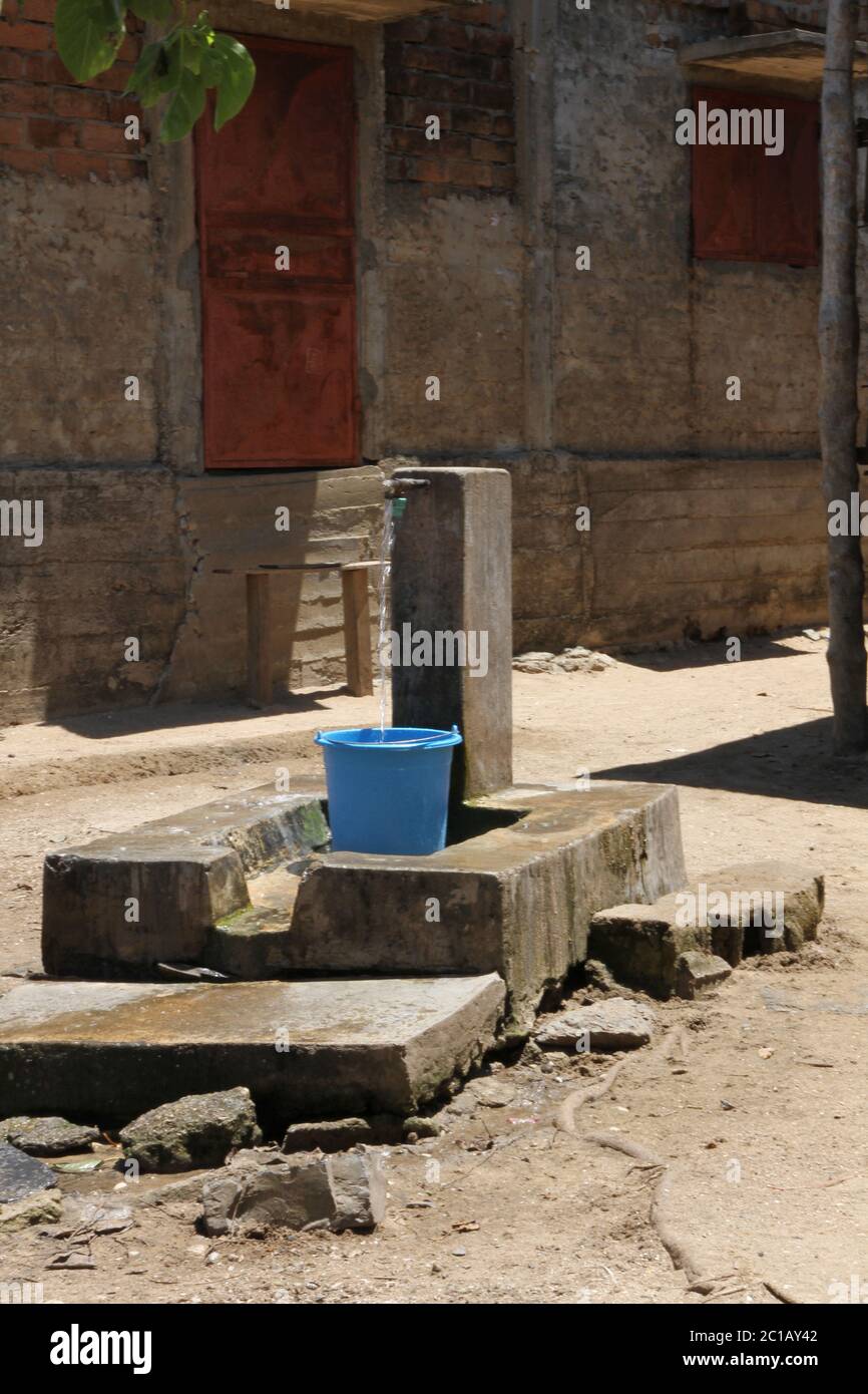 Rubinetto riempimento secchio con acqua al di fuori delle case, Ampangorinana Village, Nosy Komba Island, Madagascar. Foto Stock