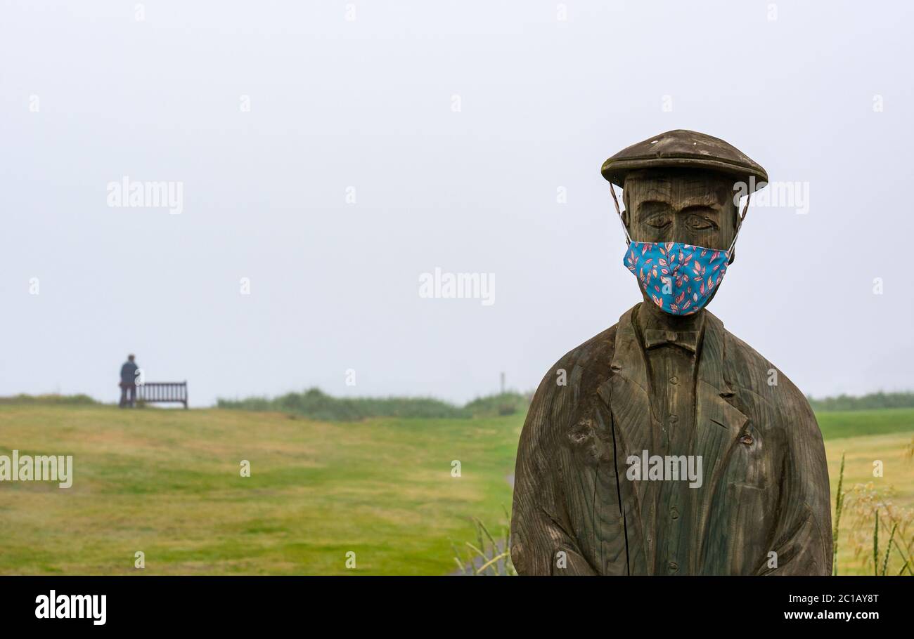 North Berwick, East Lothian, Scozia, Regno Unito, 15 giugno 2020. Regno Unito tempo: La nebbia fitta continua per il 3 ° giorno in Lothian orientale con poche persone nella popolare città di mare. Una statua in legno di ben Sayers, un giocatore di golf professionista del XIX secolo di ed Robinson, ha acquisito una maschera colorata sul Rotary Way su Elcho Green Foto Stock