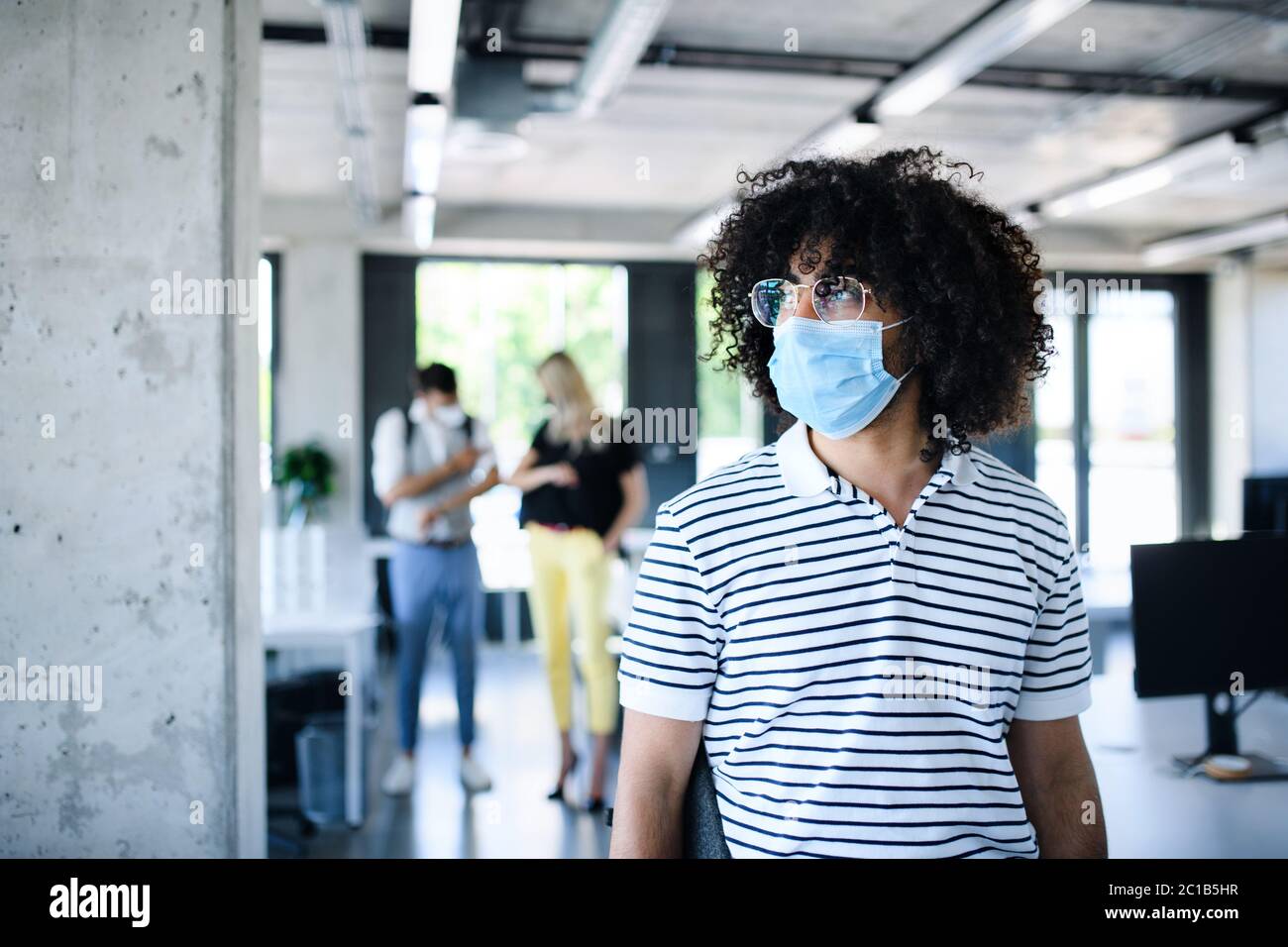 Ritratto di giovane uomo con maschera facciale di nuovo al lavoro in ufficio dopo il blocco. Foto Stock