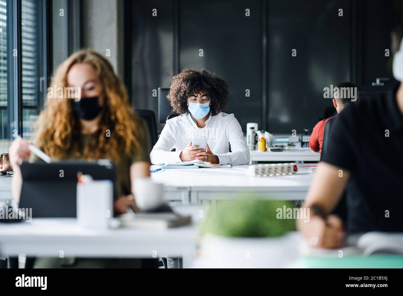 Giovani con maschere di fronte al lavoro o a scuola in ufficio dopo il blocco. Foto Stock