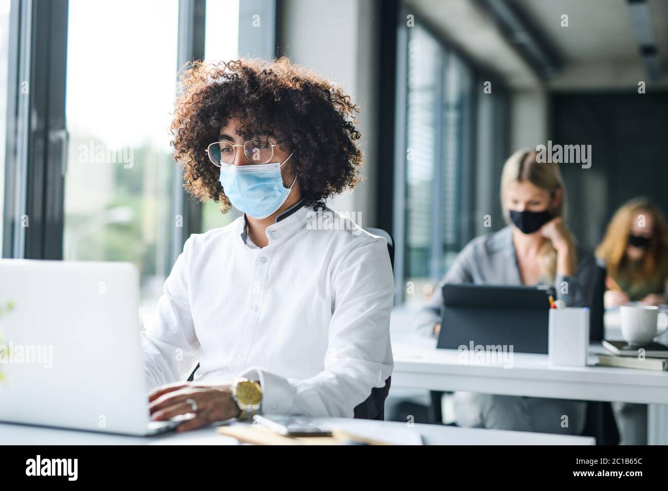 Ritratto di giovane uomo con maschera facciale di nuovo al lavoro in ufficio dopo il blocco. Foto Stock