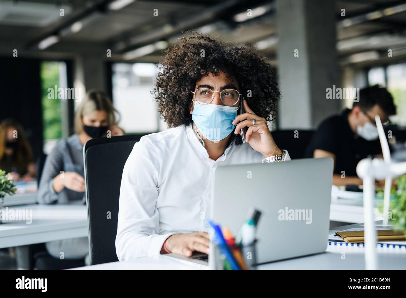 Ritratto di giovane uomo con maschera facciale di nuovo al lavoro in ufficio dopo il blocco. Foto Stock