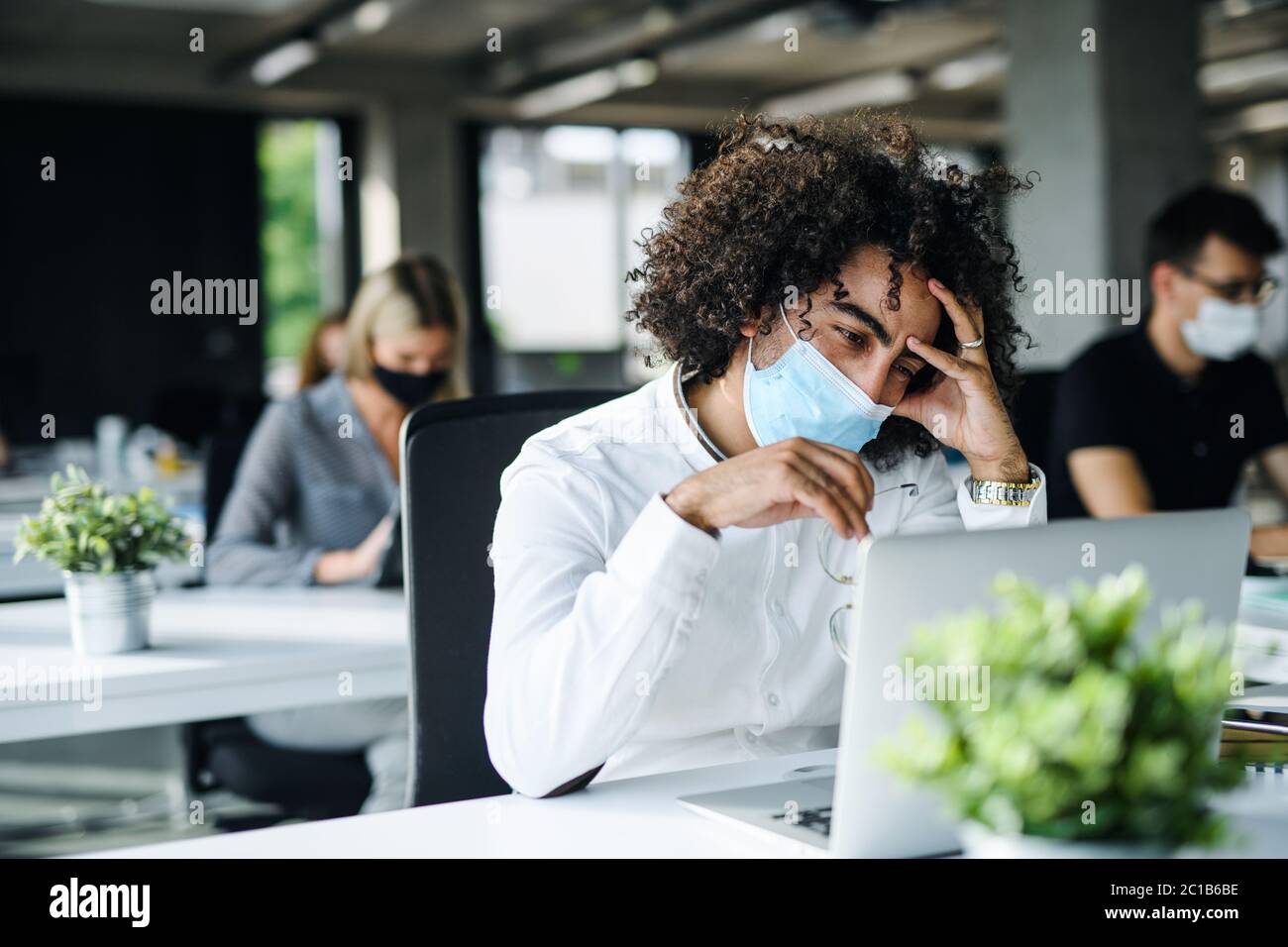 Giovane preoccupato con maschera facciale di nuovo al lavoro in ufficio dopo il blocco. Foto Stock