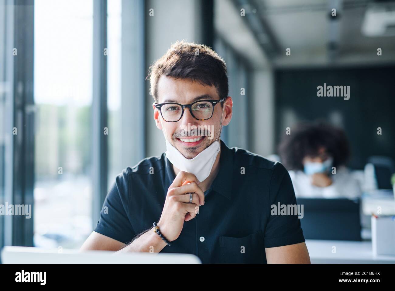 Ritratto di giovane uomo con maschera facciale di nuovo al lavoro in ufficio dopo il blocco. Foto Stock