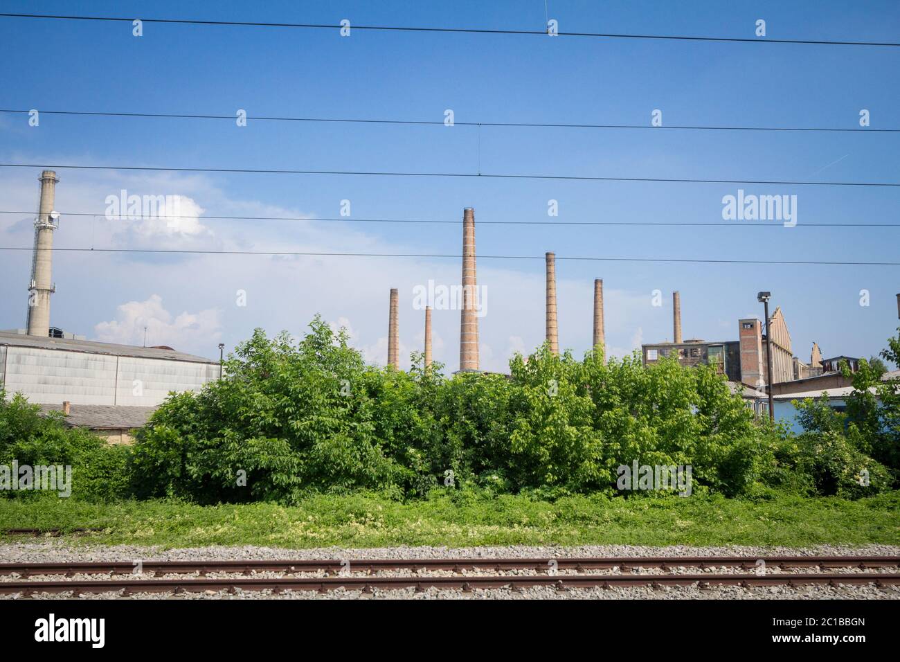 Panorama di un complesso industriale abbandonato con i suoi tipici alti camini in mattoni rossi mentre cavi e binari ferroviari sono visibili di fronte, dentro Foto Stock