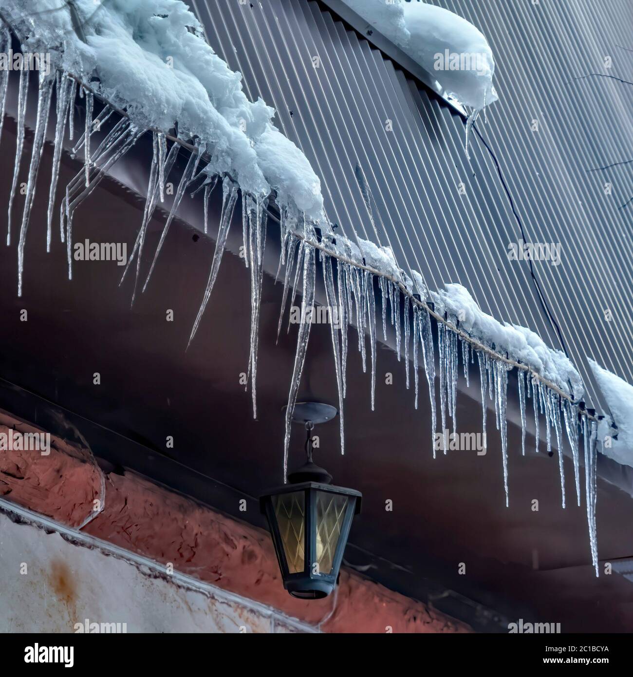 Ghiaccio a chiocciole quadrate al bordo del tetto grigio con grumi di neve in inverno Foto Stock