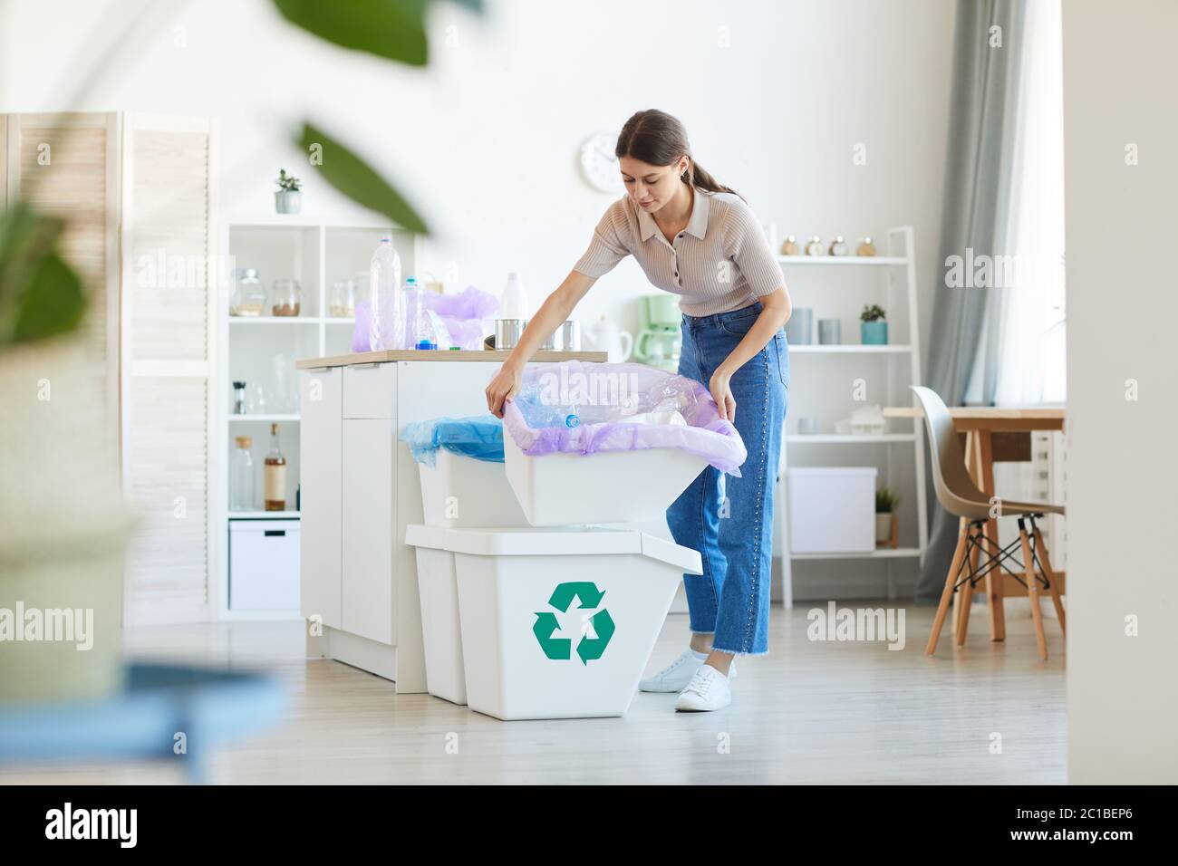 Giovane donna che getta fuori la spazzatura che porta i bidoni in cucina Foto Stock
