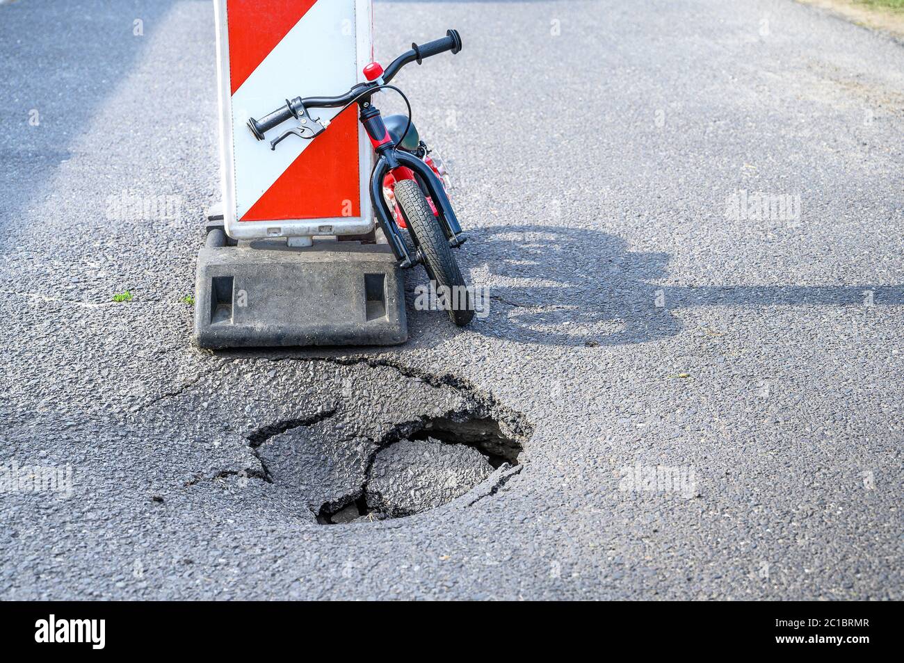 Balance bike (push bike) si appoggia contro deviazione segnale di allarme traffico vicino a pothole su strada asfaltata con Foto Stock