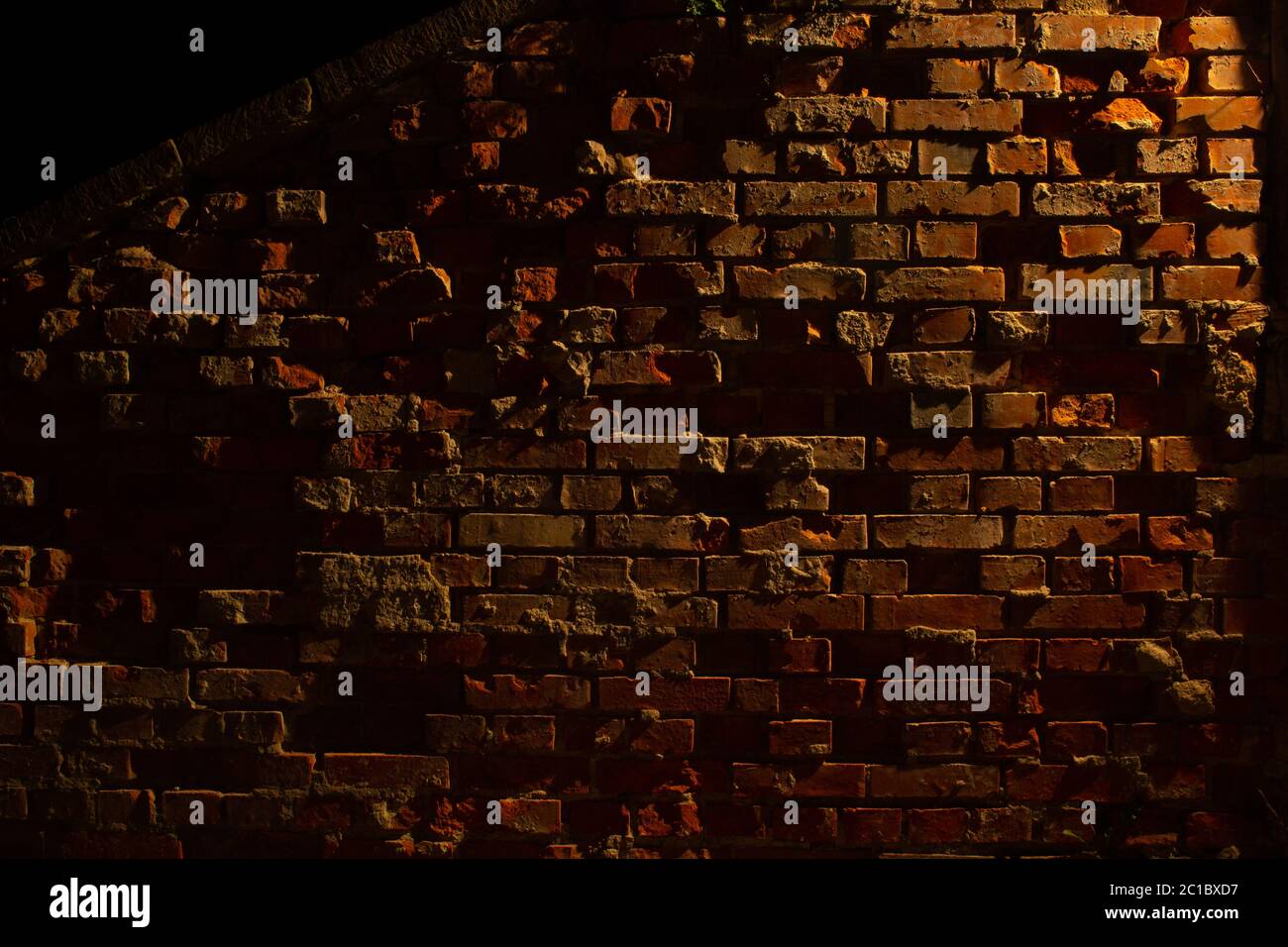 Vecchia grugia e muro di mattoni rossi danneggiato di notte con luce di una lanterna che splende su di essa Foto Stock