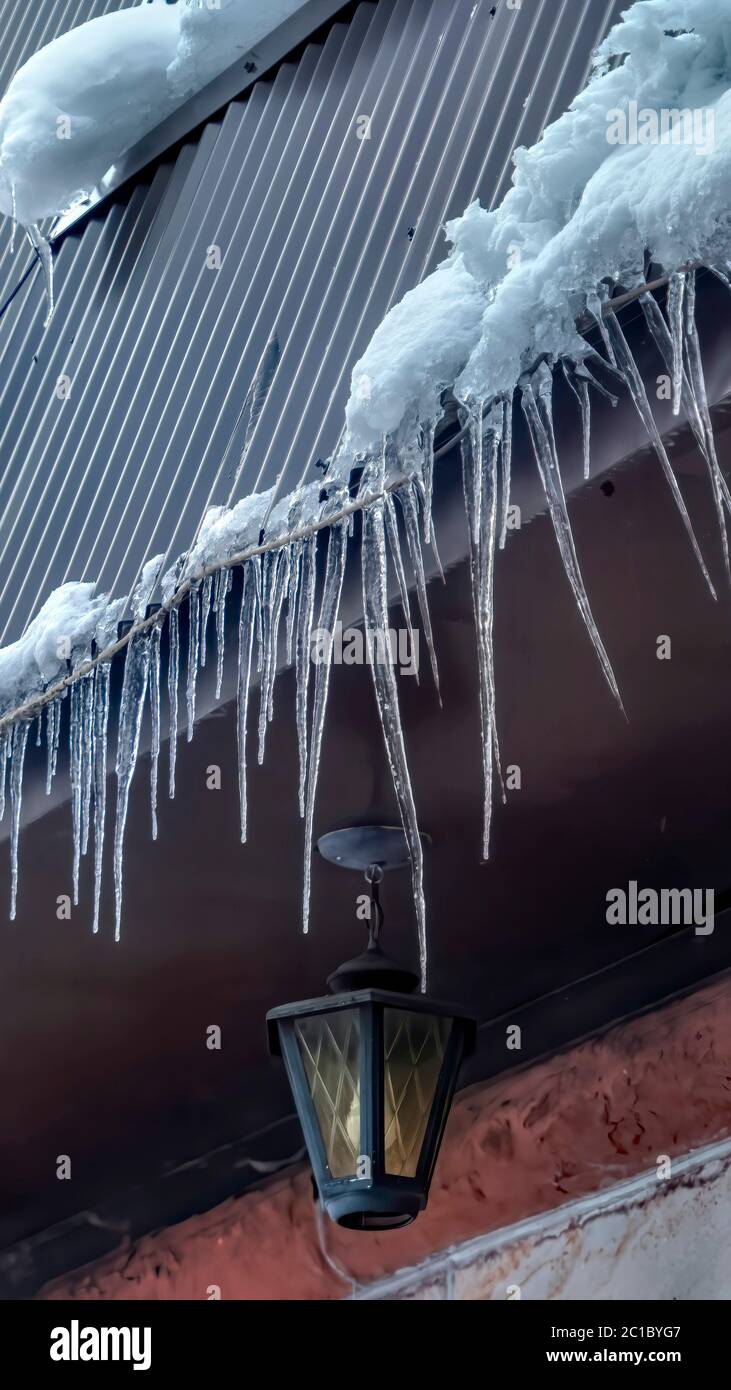 Telaio verticale picicles con punte al bordo del tetto grigio con pitched grumi di neve in inverno Foto Stock