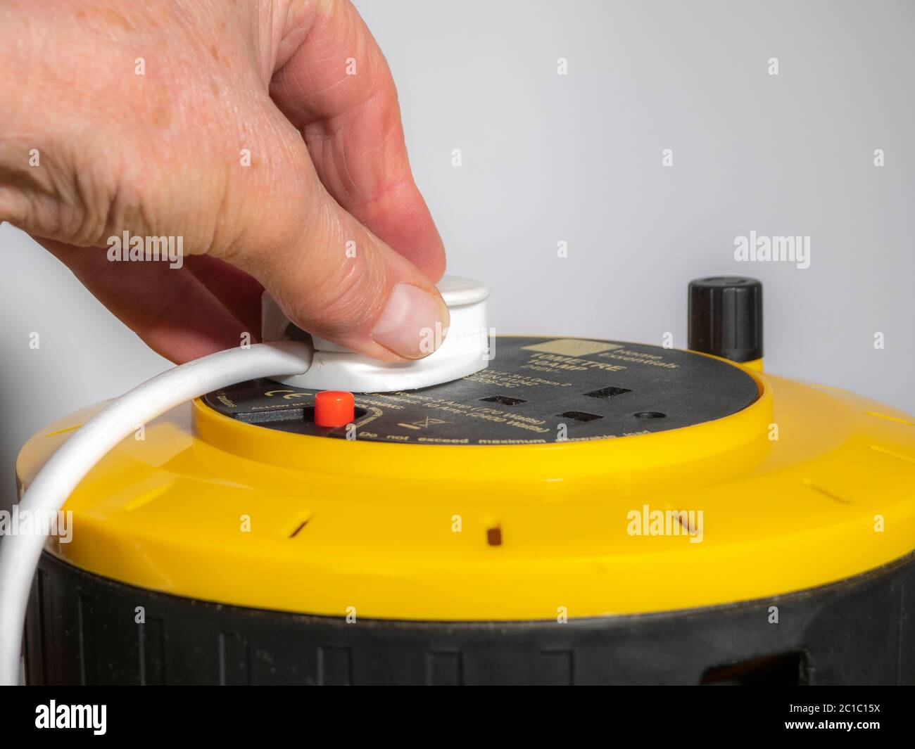 Mano dell'uomo su una spina inglese a tre pin, inserita in una presa elettrica da 240 volt su un'estensione dell'alimentatore da 10 metri, con cavo avvolto su un aspo. Foto Stock