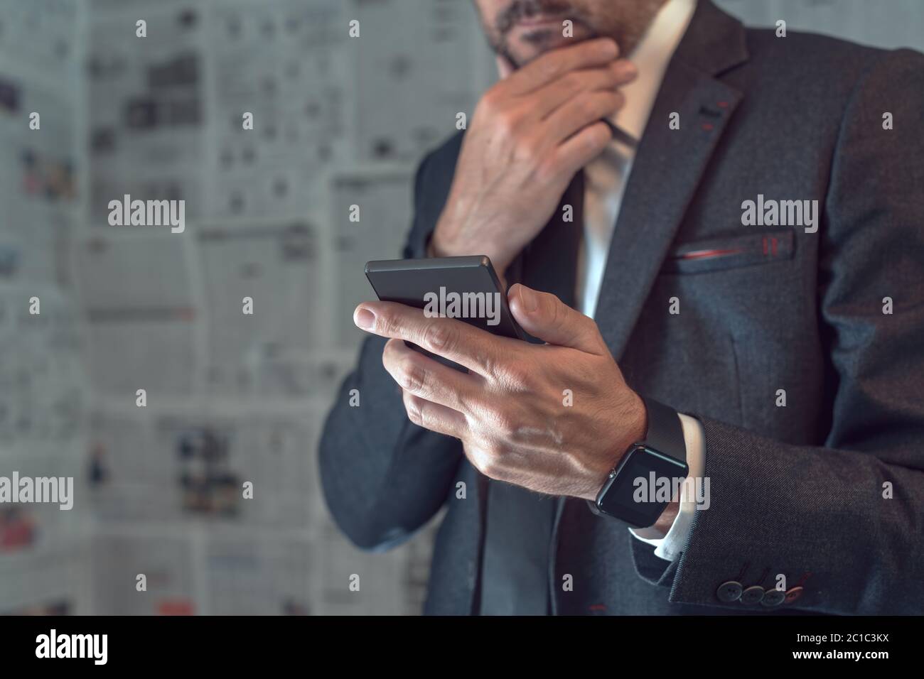 Uomo d'affari che usa il telefono cellulare in concetto infodemico di notizie false con pagine tabloid del giornale in background Foto Stock