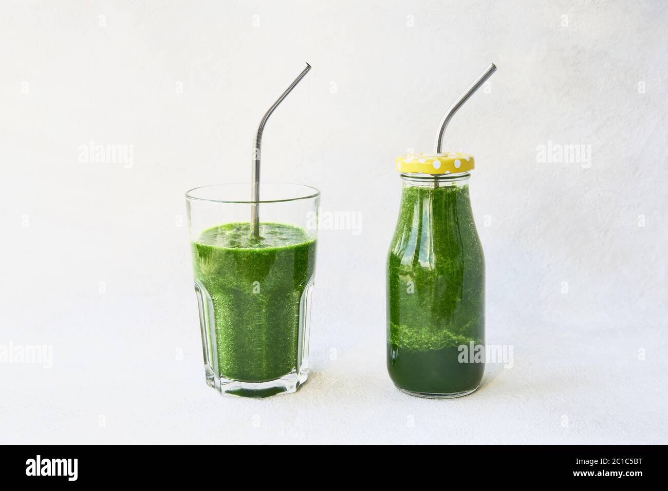 Frullato verde con spinaci in bottiglia piccola e in bicchiere da bere con paglia metallica. Spazio di copia per il testo. Concetto di stile di vita sano Foto Stock