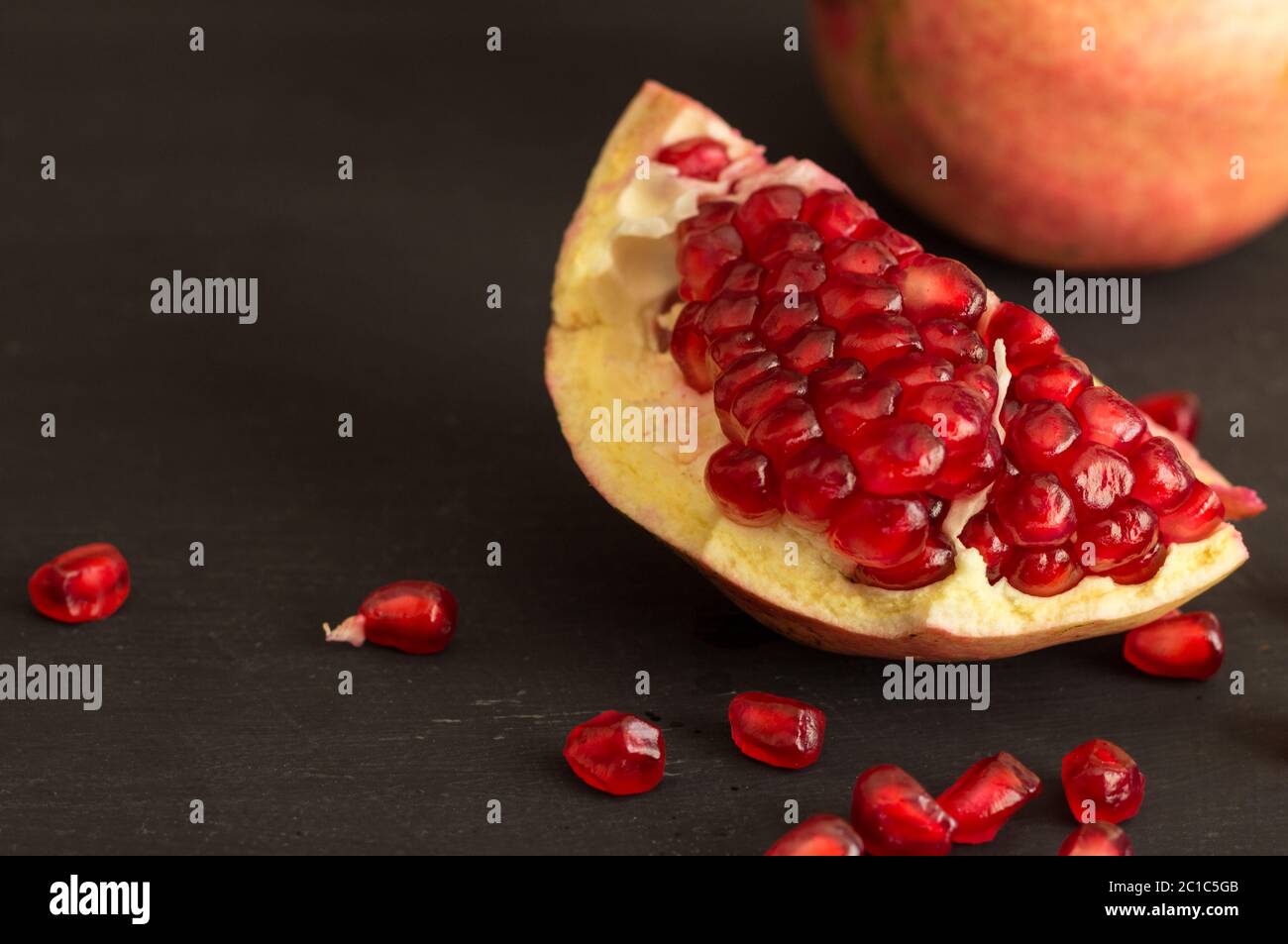 Melograno fetta di frutta e semi di vita ancora rustico sfondo nero Foto Stock