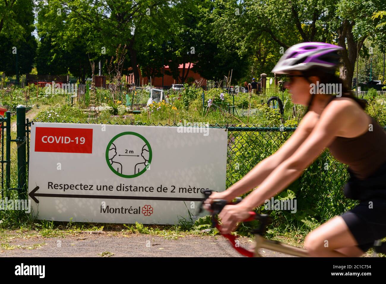 Verdun, CA - 14 Giugno 2020 : Donna che cavalcano una bicicletta davanti al cartello riportante le linee guida francesi di sicurezza Covid-19 Foto Stock