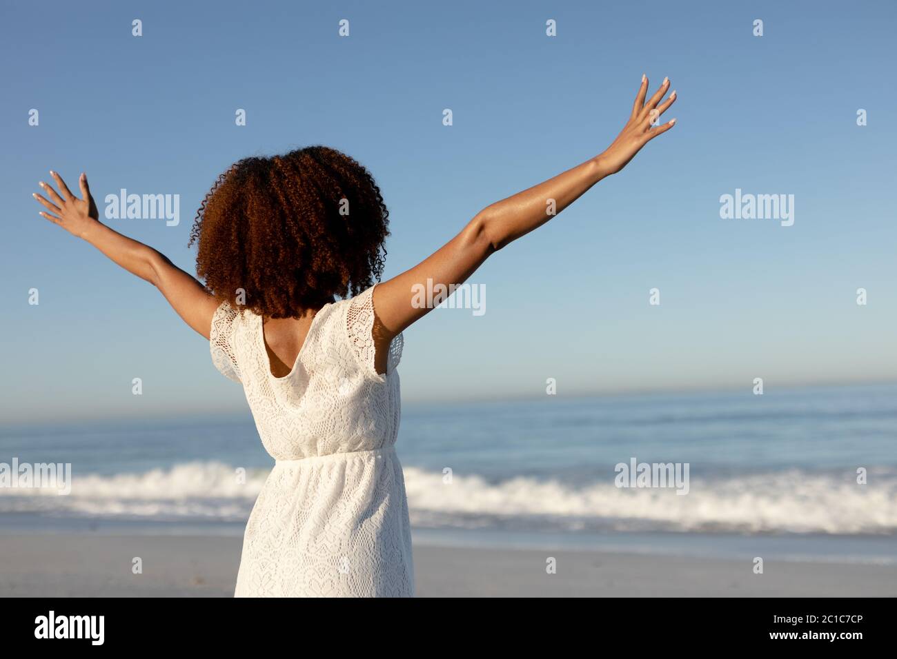 Una donna mista da corsa con le braccia distese sulla spiaggia in una giornata di sole Foto Stock