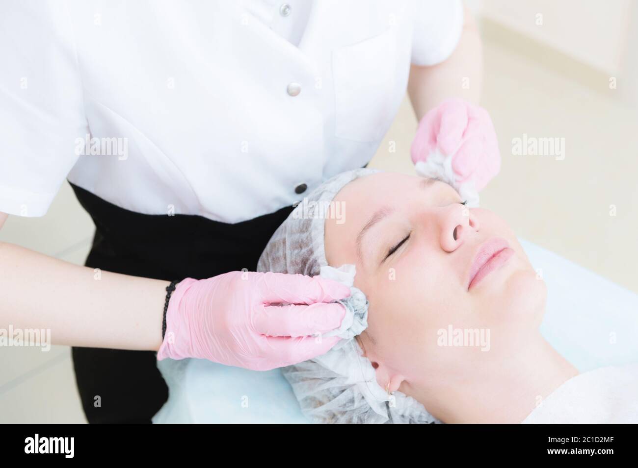 Un primo piano della procedura di pulizia nell'ufficio di cosmetologia. Le mani del cosmetologo in guanti rosa vengono rimosse Foto Stock