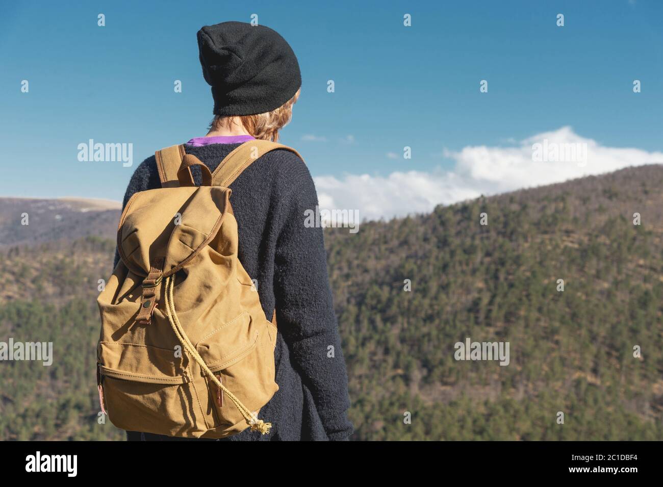 Una fotografa di viaggio hipster ragazza in un cappello e con uno zaino in piedi su una roccia e guardando le colline. Foto Stock