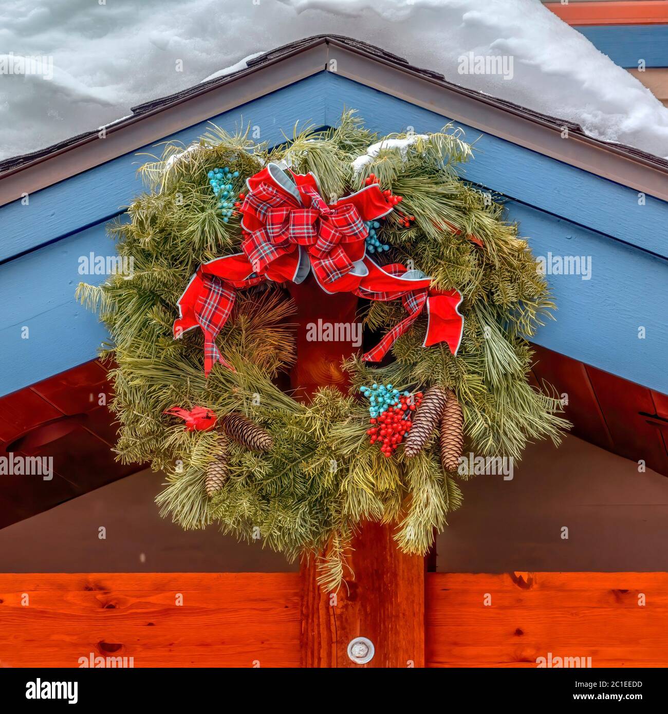 Corona di Natale quadrata fatta di foglie sempreverdi contro il tetto innevato Foto Stock