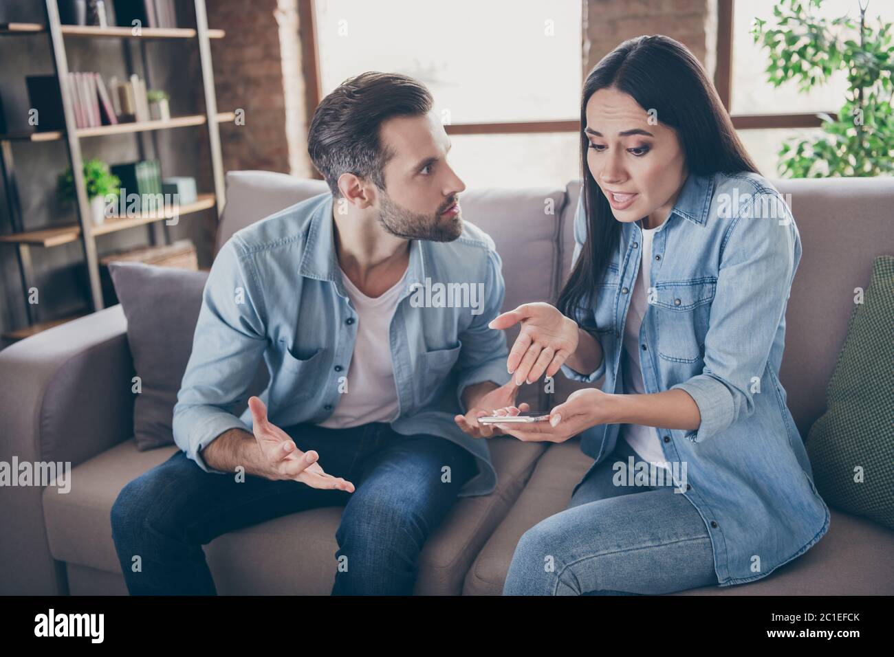Foto di due persone donna uso smartphone provare a spiegare invidia arrabbiato marito non ha un altro uomo punto mano schermo sentire confuso sedersi comfort accogliente Foto Stock