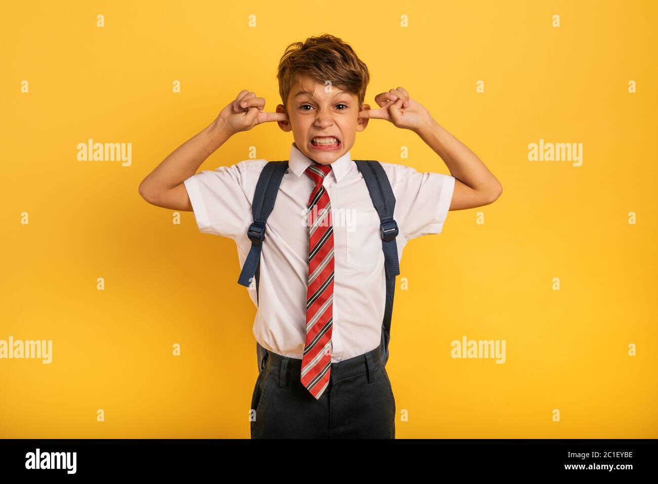 Studente Bambino copre le orecchie perché non vuole sentire il rumore. Sfondo giallo Foto Stock