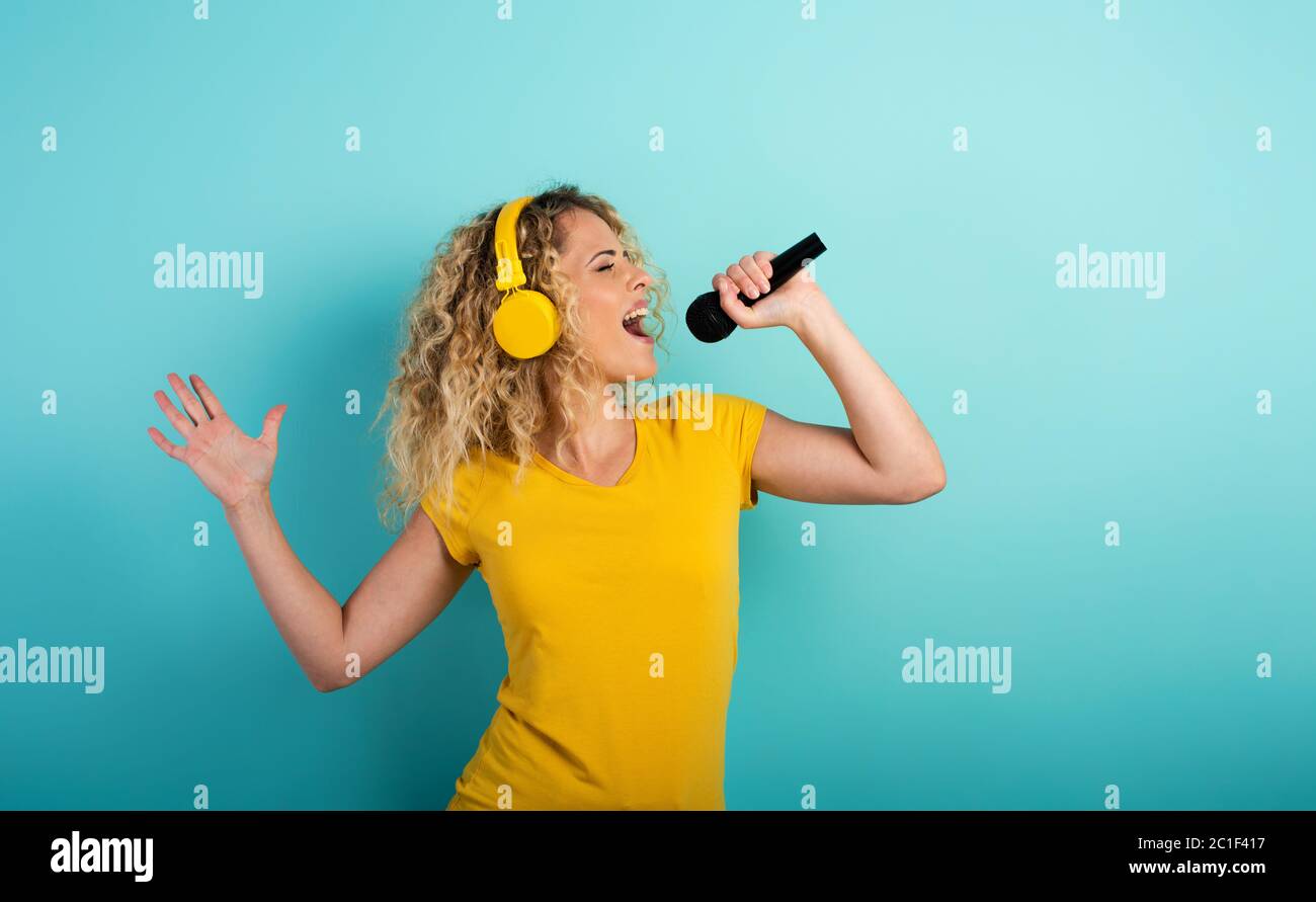 Ragazza con cuffia ascolta musica e canzone con microfono. Espressione emotiva ed energetica. Sfondo ciano Foto Stock