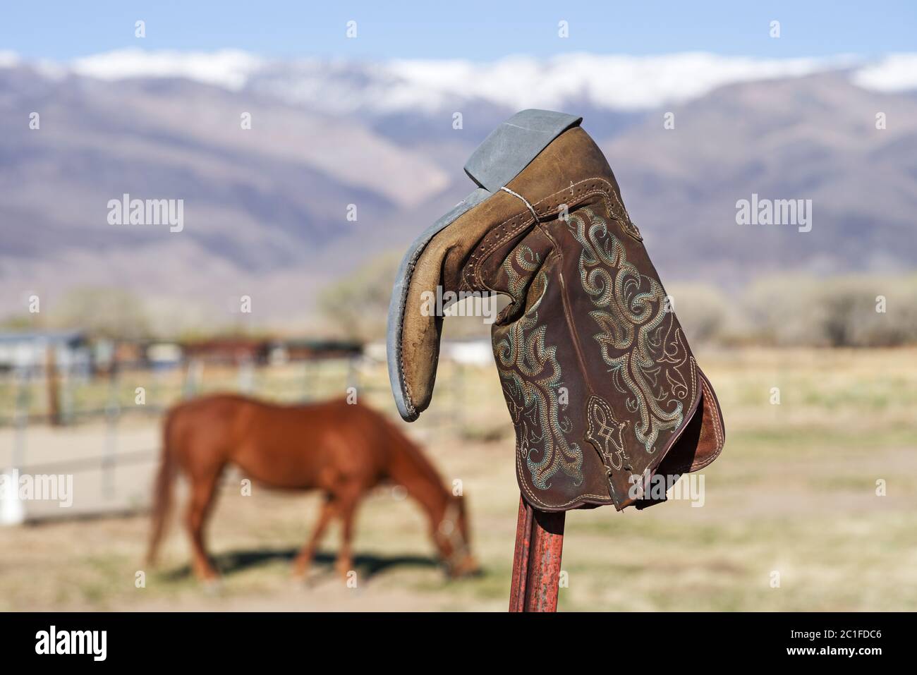 vecchio stivale da cowboy sul fincepad con cavallo fuori fuoco e montagna in background Foto Stock