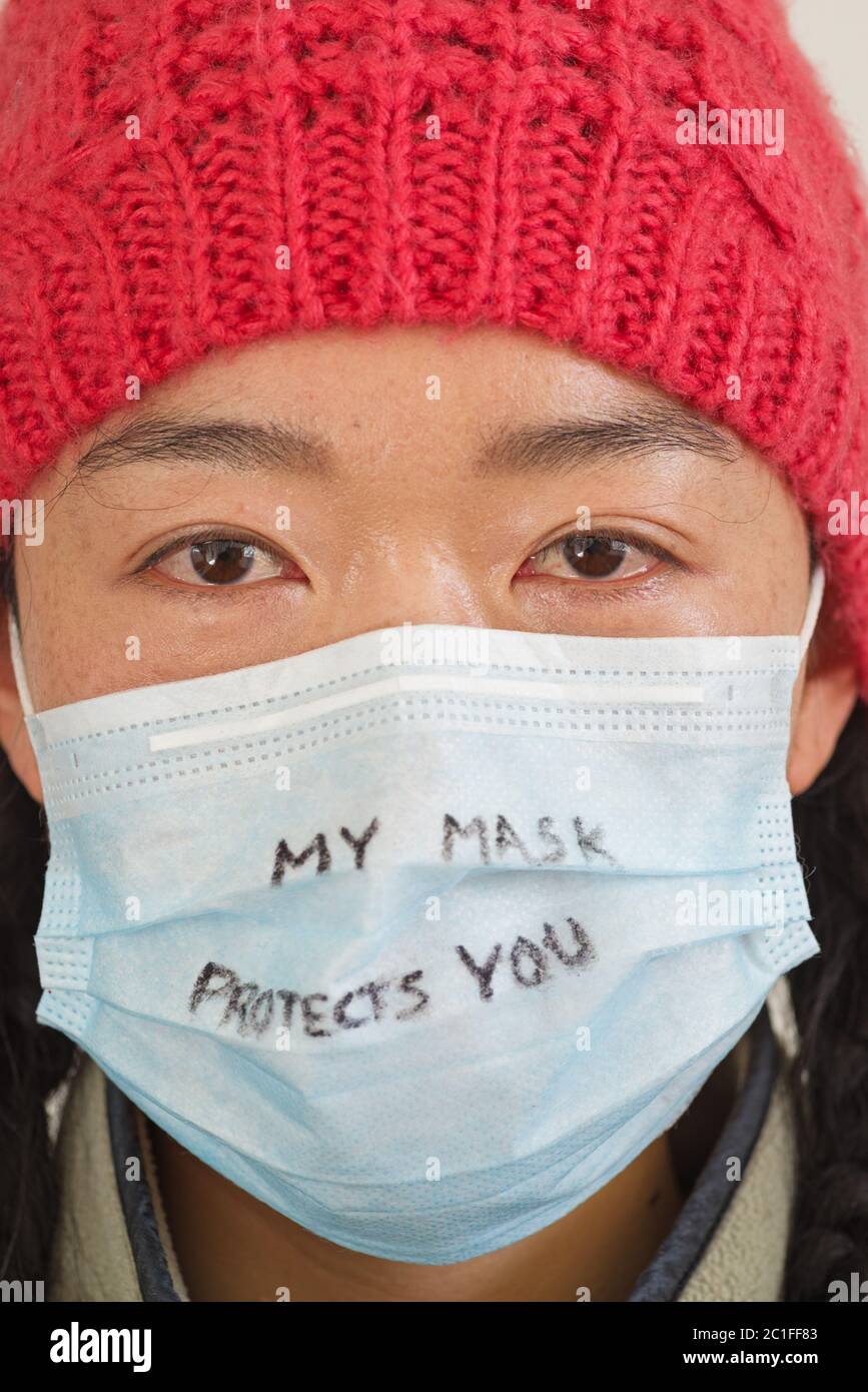 Donna asiatica con la mia maschera ti protegge scritto in marker sulla sua maschera facciale Foto Stock