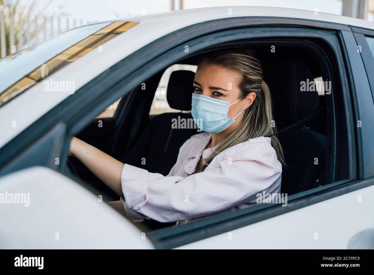 Donna con maschera facciale che guida la sua auto durante la pandemia di coronavirus Foto Stock