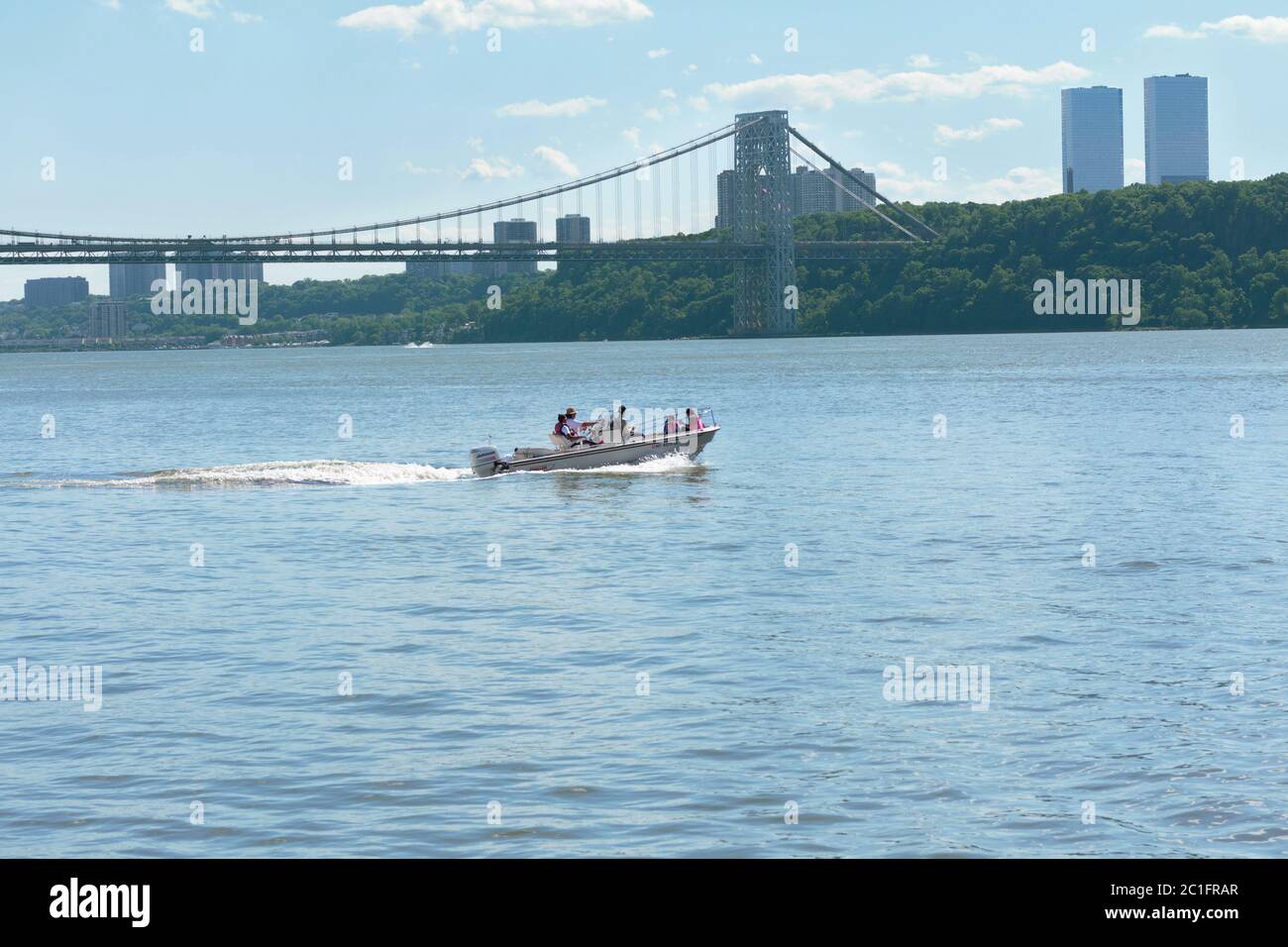 Una barca piena di persone si muove attraverso il fiume Hudson con il George Washington Bridge e lo skyline del New Jersey sullo sfondo Foto Stock