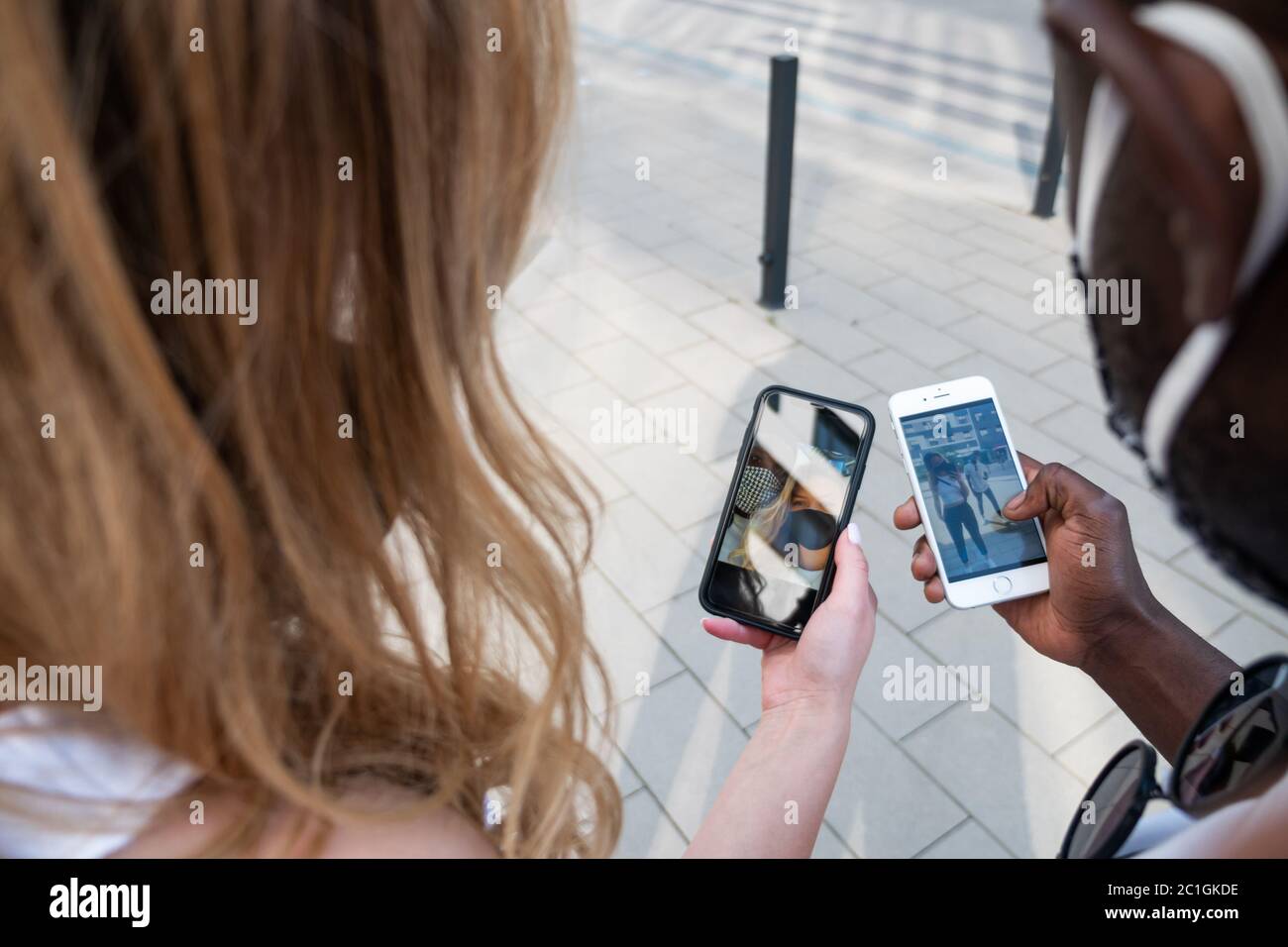 Coppia mista che condivide le immagini sugli schermi del telefono. All'aperto. Vista sulla spalla. Foto Stock