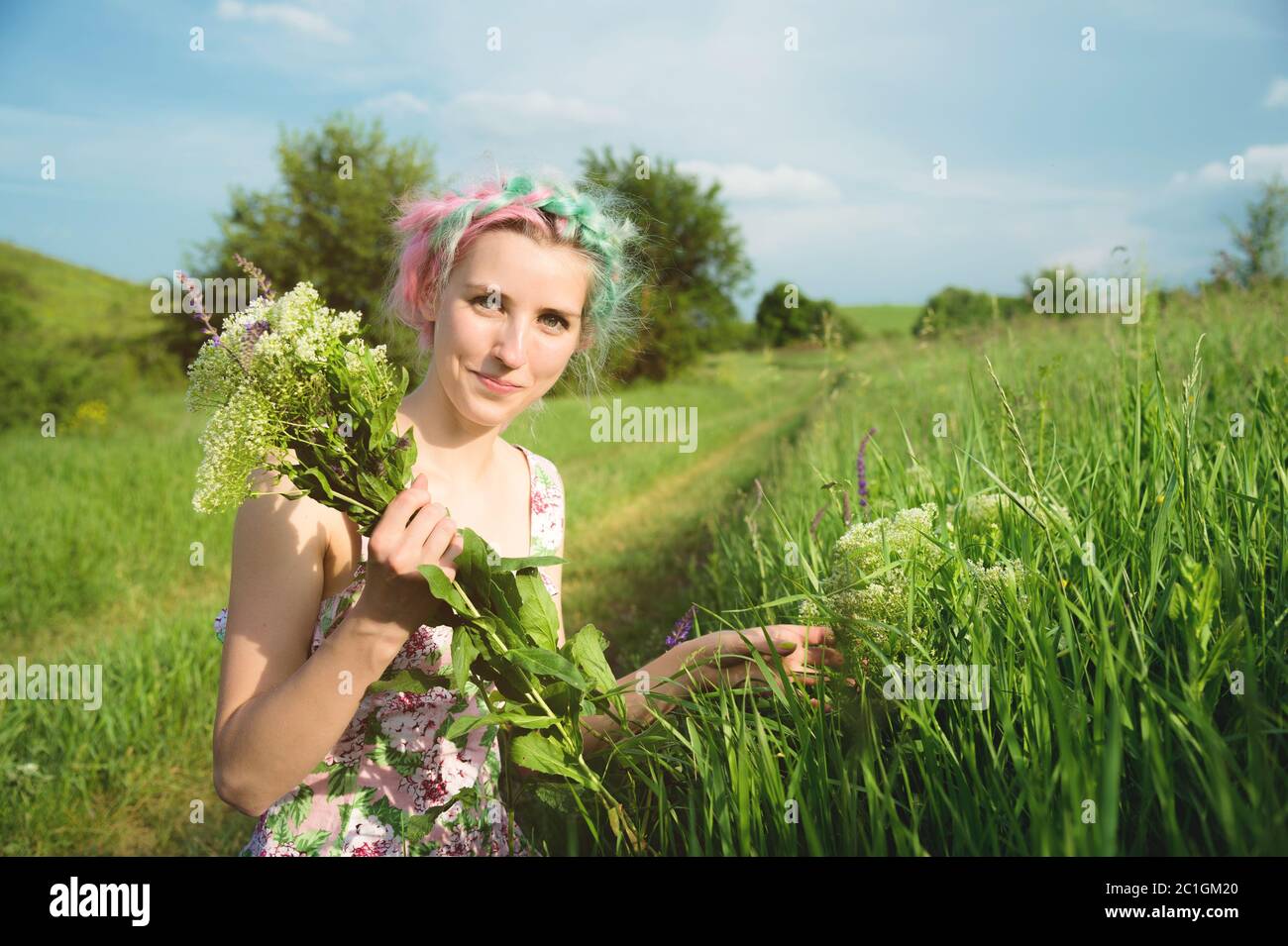 Ritratto di una ragazza giovane e carina felice con capelli multicolore raccoglie fiori accanto a una strada di campagna al tramonto. Il concetto di hu Foto Stock