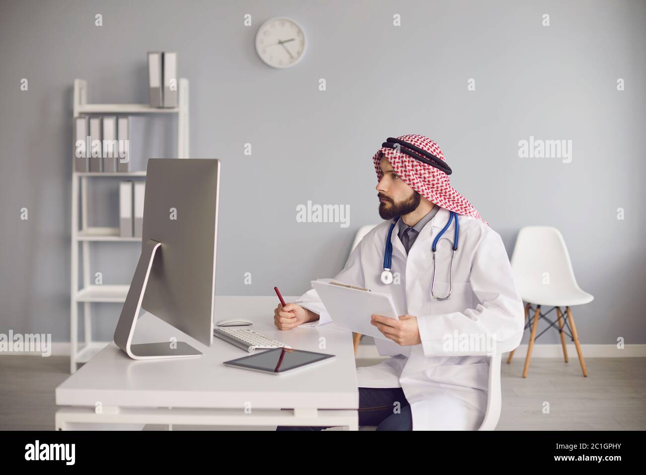 Giovane medico etnico che lavora con il computer in ufficio Foto Stock