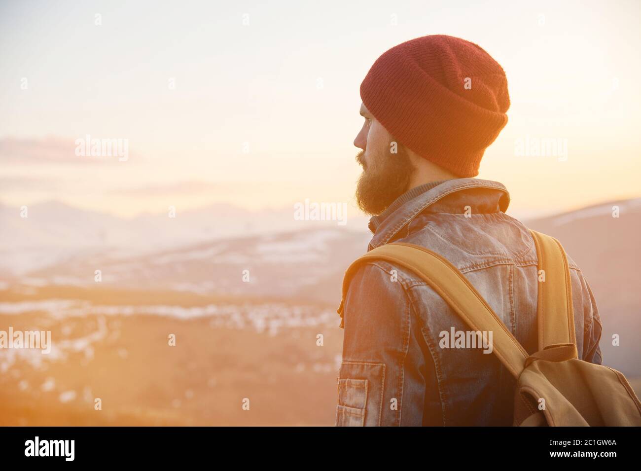 Uomo hipster turistico con un cappello con uno zaino si trova su una strada di ritorno e guardare il tramonto contro lo zaino Foto Stock