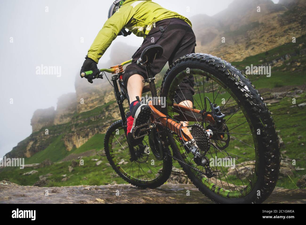 Gambe di ciclisti e ruote posteriori vista ravvicinata della moto mtb posteriore in montagna sullo sfondo di rocce in condizioni atmosferiche nebbie. Il c Foto Stock