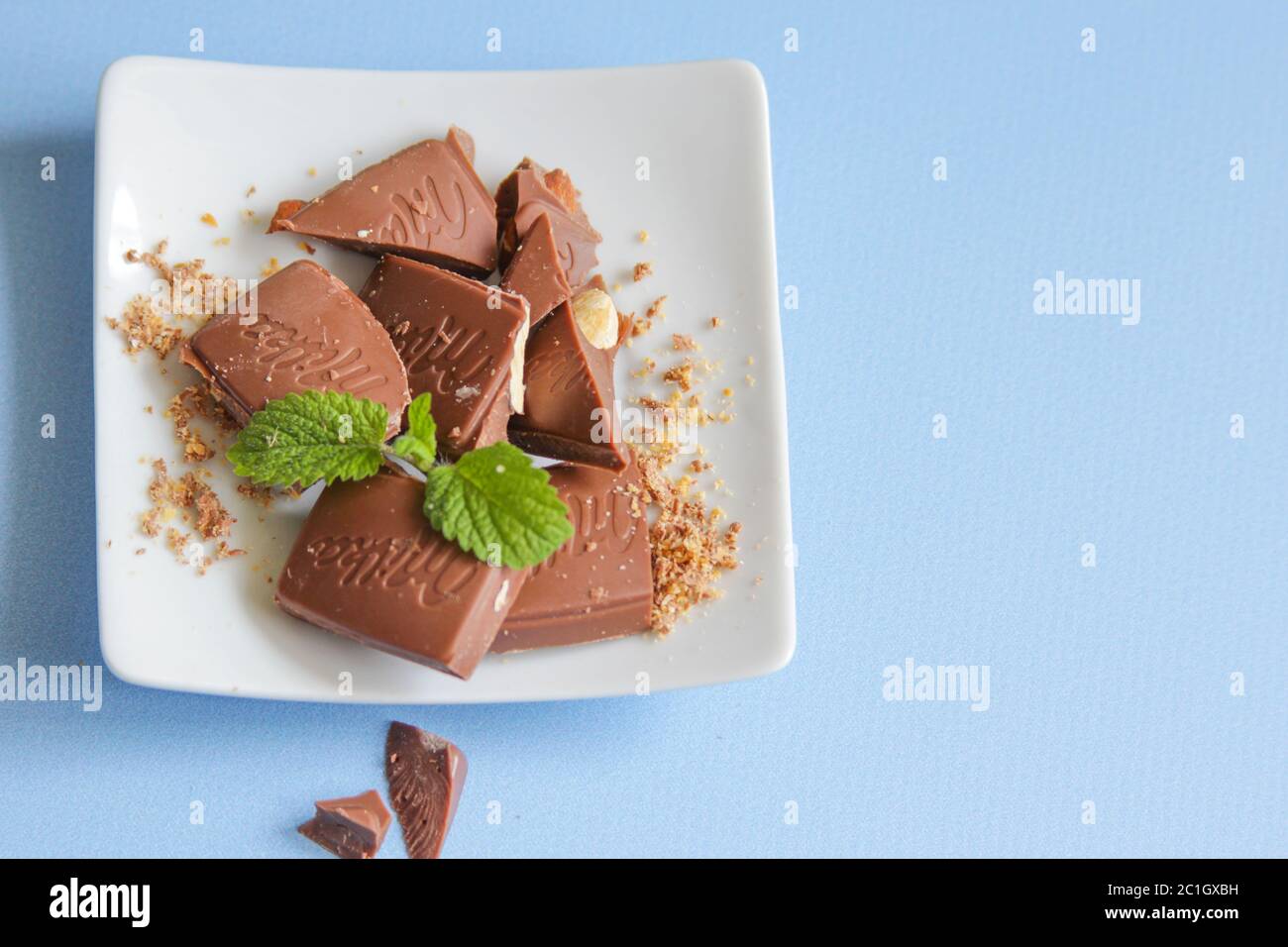 Milka al cioccolato al latte con una foglia di menta fresca sul fondo blu. Foto Stock