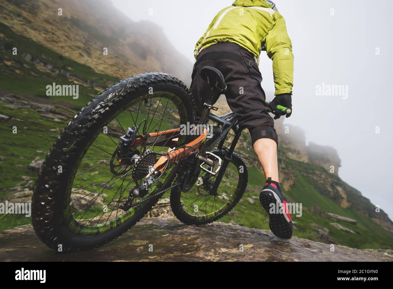 Gambe di ciclisti e ruote posteriori vista ravvicinata della moto mtb posteriore in montagna sullo sfondo di rocce in condizioni atmosferiche nebbie. Il c Foto Stock