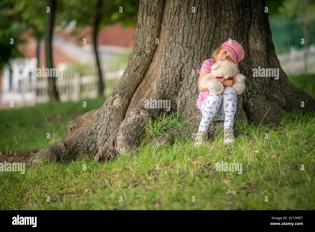 Ragazza seduta sotto un albero che tiene orsacchiotto Foto Stock