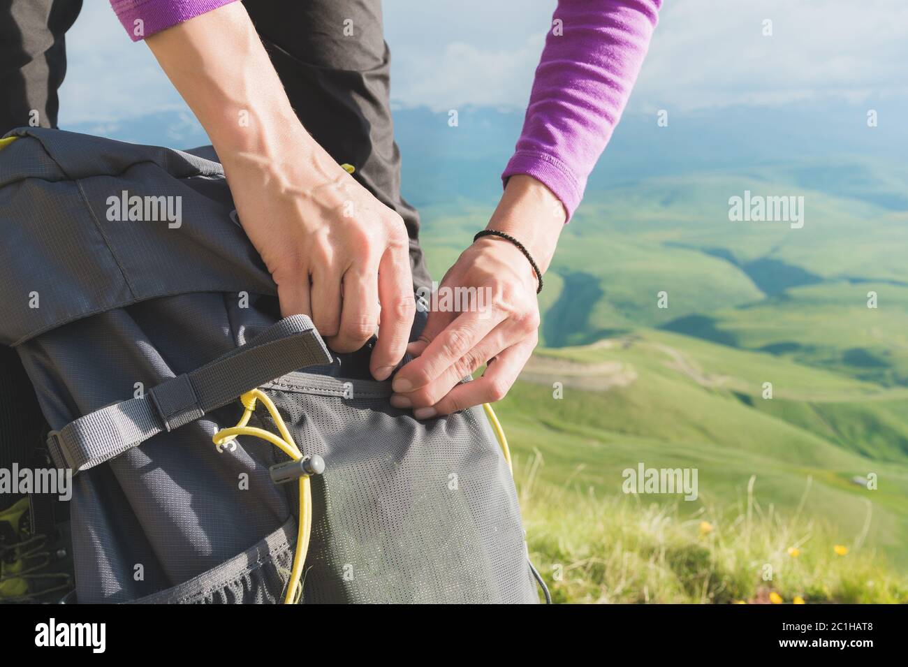 Primo piano delle mani delle donne sallacciano la fibbia sullo zaino del campo sullo sfondo della valle nel sole che tramonta. Tour Foto Stock