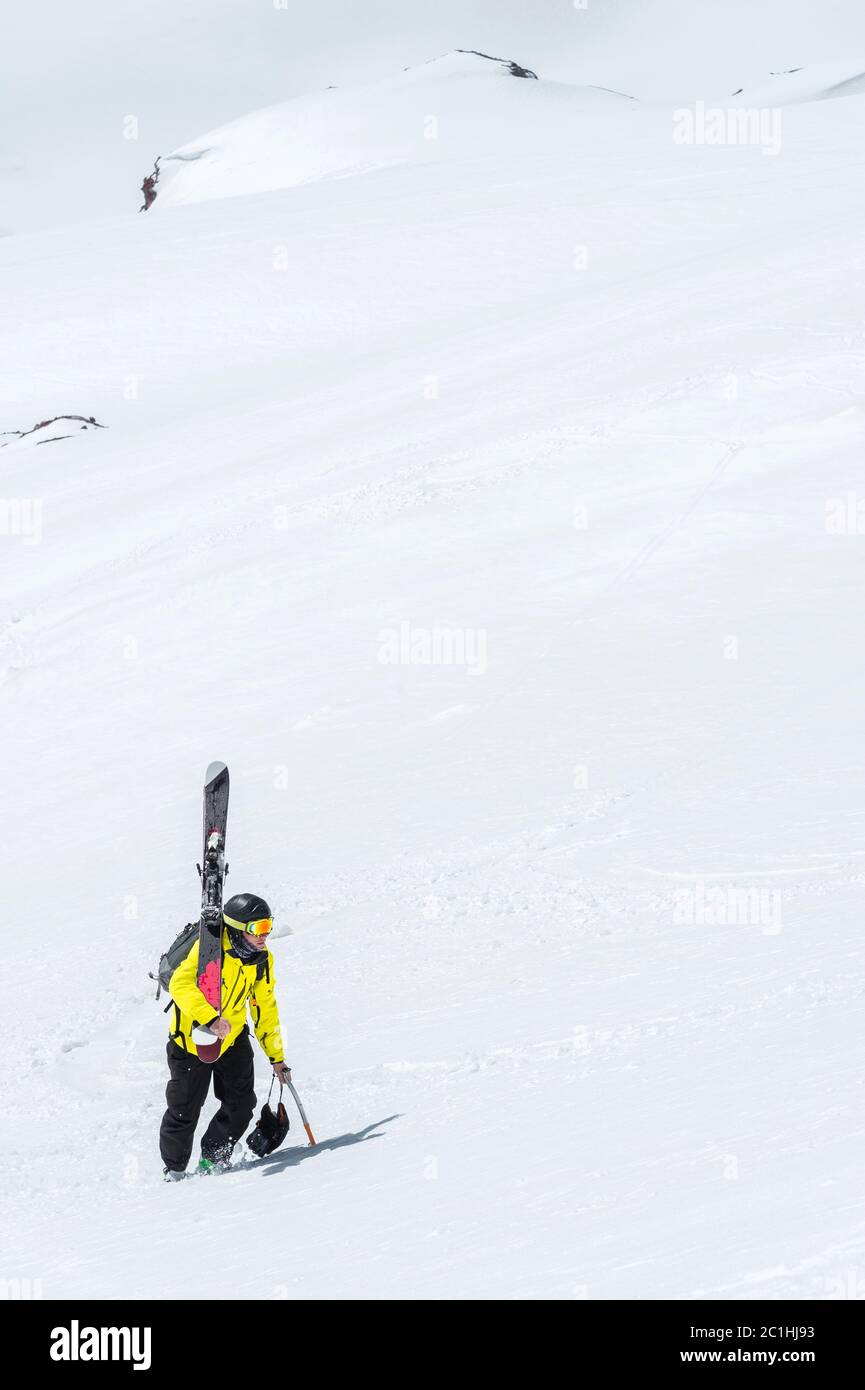 Uno sciatore in un casco e maschera con uno zaino si erge su un pendio sullo sfondo della neve e di un ghiacciaio. Freeride backcountry Foto Stock
