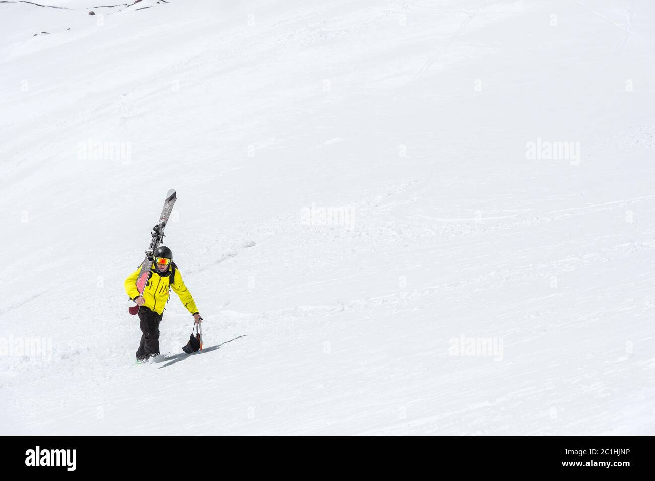 Uno sciatore in un casco e maschera con uno zaino si erge su un pendio sullo sfondo della neve e di un ghiacciaio. Freeride backcountry Foto Stock