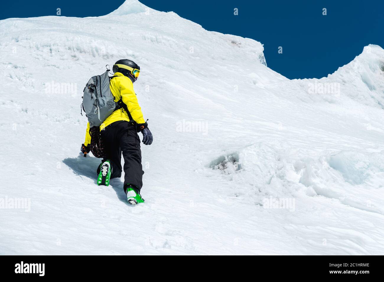 Uno sciatore in un casco e maschera con uno zaino si erge su un pendio sullo sfondo della neve e di un ghiacciaio. Freeride backcountry Foto Stock