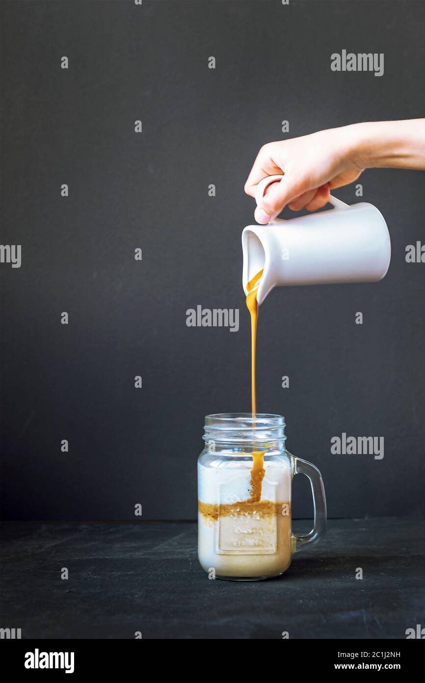 La schiuma di caffè viene versata in una tazza con latte. Preparazione del caffè Dalgona. Sfondo nero, primo piano Foto Stock